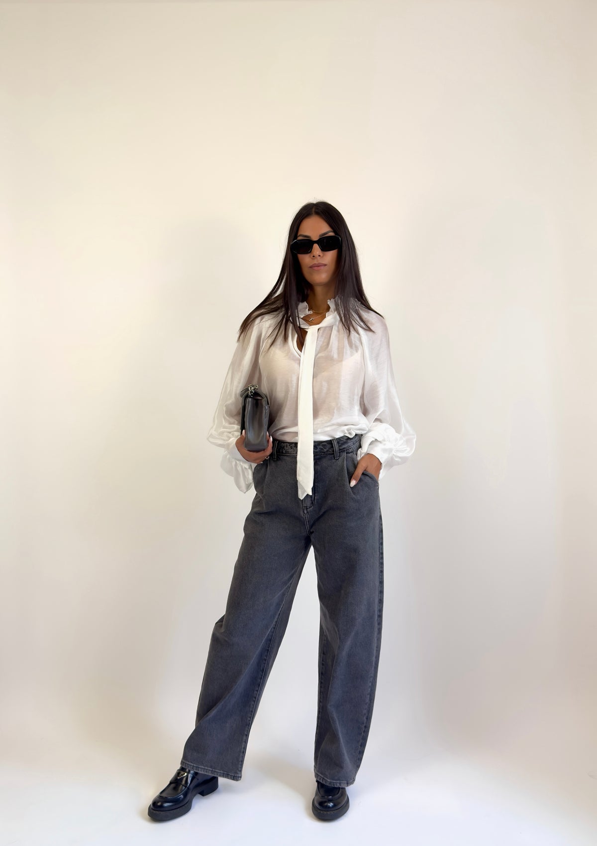 Camicia elegante bianca con fiocco al collo e maniche ampie, indossata con jeans balloon grigi.