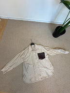 Camicia beige del coordinato Riviera con maxi tasca scura intrecciata a contrasto, vista frontale.