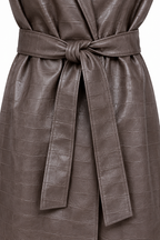 Dettaglio della cintura annodata del cappotto marrone effetto pelle.